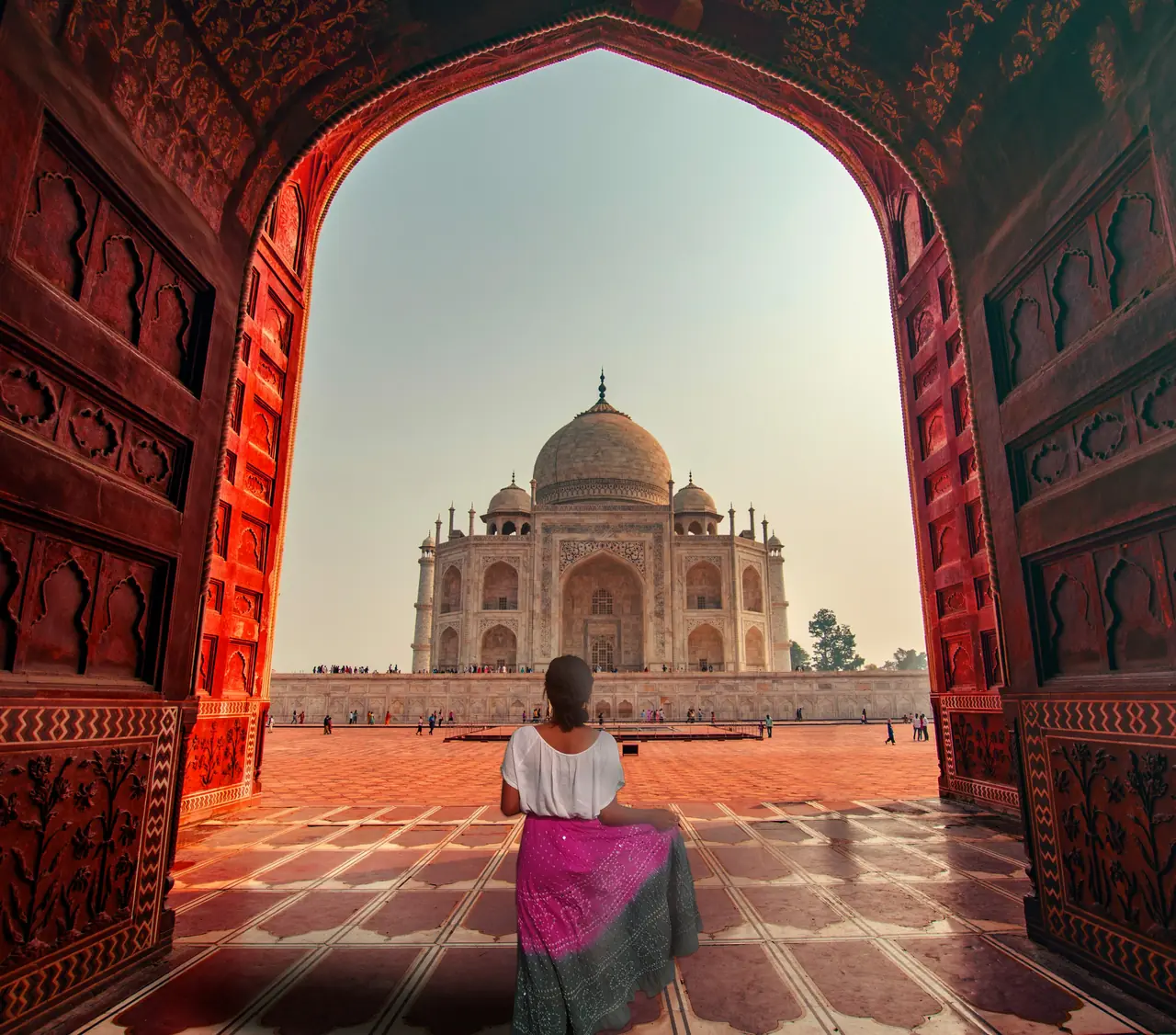 A traveller looking at the Taj Mahal through a red sandstone arch